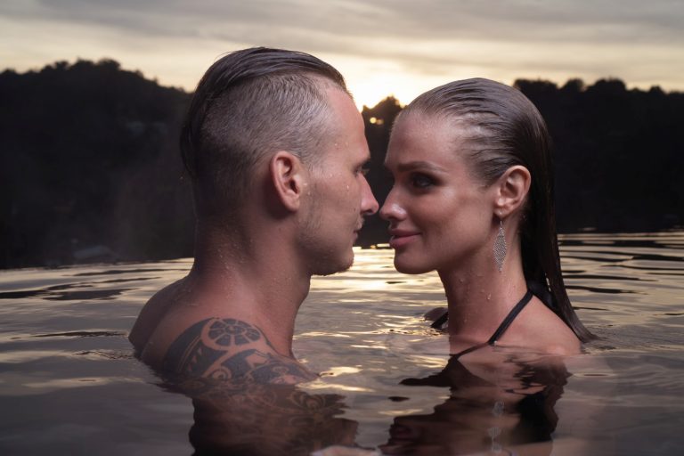 Romantic sensual couple alone in infinity swimming pool over beautiful tropical and sunset sky background