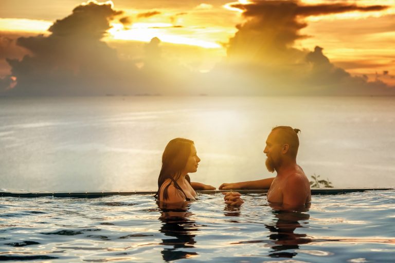 Romantic couple in the infinity pool at sunset overlooking the sea and sunset